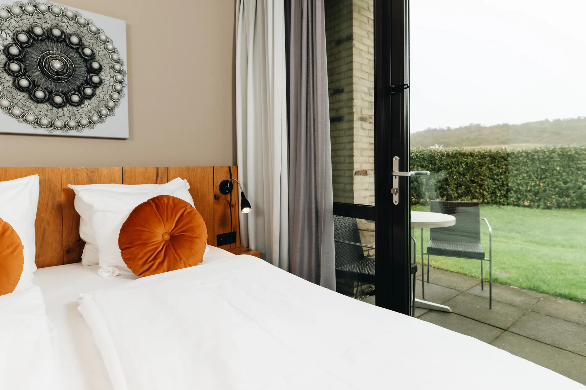 Detailopname van een comfortabel hotelbed met oranje accenten en een openstaande terrasdeur die zorgt voor een natuurlijke lichtinval.